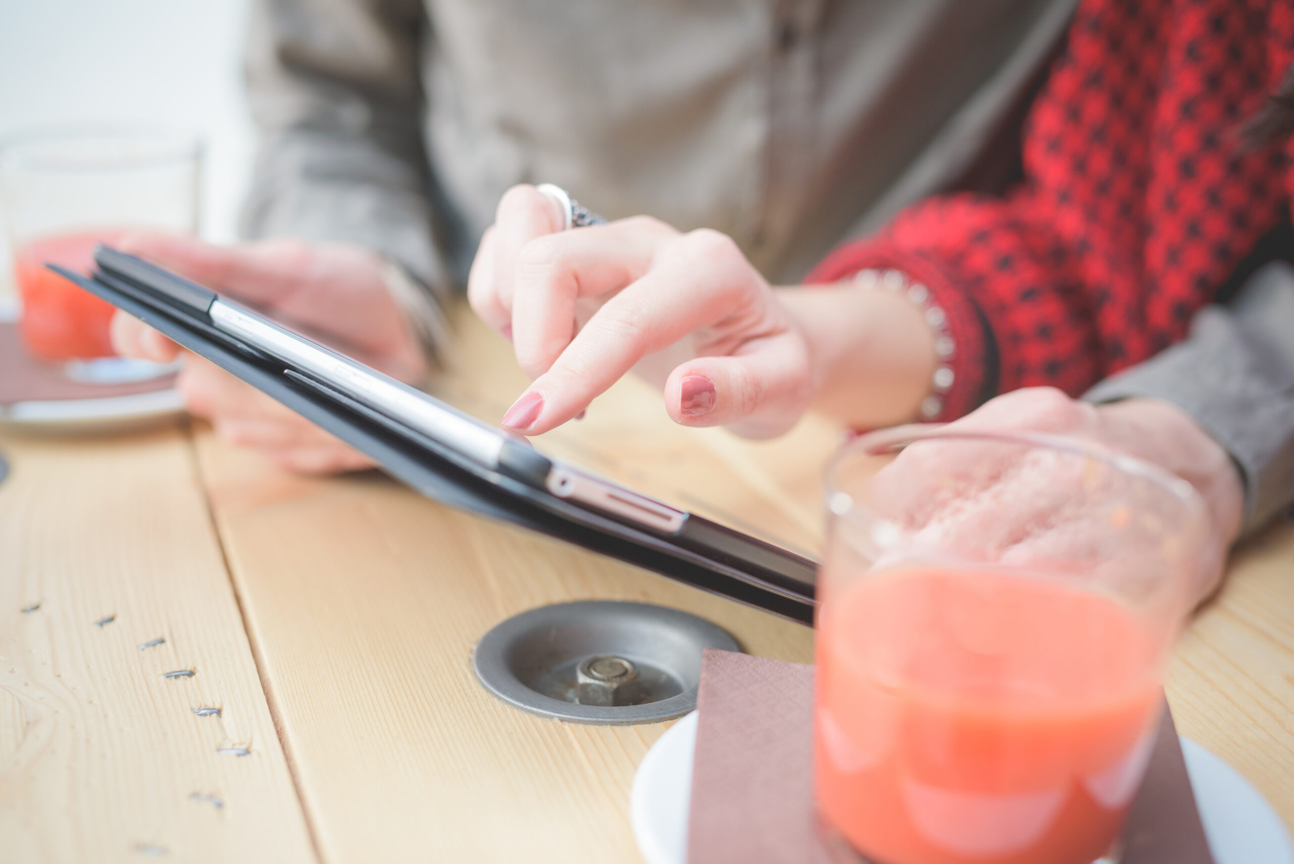 Close-up of hands touching digital tablet, informal businesswoman and businessman with cups of juice on table - business, work, technology concept